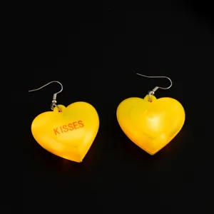 Dettaglio di orecchini a cuore LED gialli con stampa kisses ideali per feste.
