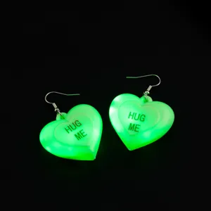 Dettaglio in primo piano dei luminosi orecchini a cuore verde con LED e scritta HUG ME.