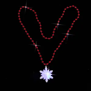 Close-up of red beaded necklace with glowing LED snowflake pendant for holiday decoration.