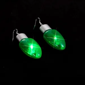 Détail en gros plan des boucles d'oreilles ampoule lumineuse verte, bijoux de Noël LED fun.
