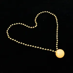 Close-up detail of glowing yellow ball pendant and gold bead chain on black background.