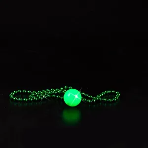 Close-up detail shot of the glowing green ball pendant and beaded chain in dark ambiance.