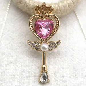 Close-up of gold magical wand pendant with pink heart crystal and pearls for DIY jewelry making.