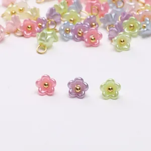 Closeup detail of mini resin pearlescent flower charms with golden loops for DIY bracelet making.