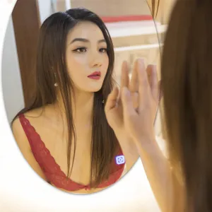 Close-up detail of the smart oval LED bathroom mirror reflecting a model with warm light.