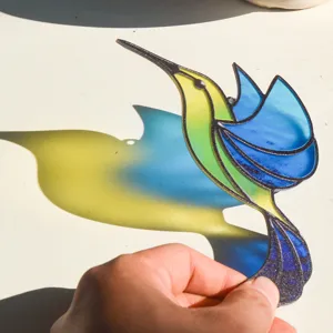 Closeup of colorful hummingbird acrylic suncatcher casting vibrant light shadow in direct sunlight.