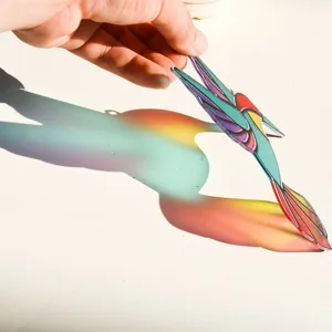Acrylic hummingbird suncatcher detail showing vibrant rainbow light refraction effect indoors.