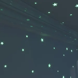 Glowing star stickers close up in dark room, fluorescent wall decor for kids bedroom ceiling.