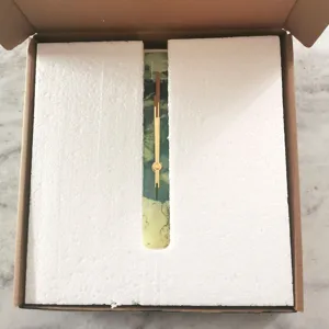 Detail view of the modern acrylic wall clock packaging with gold hands inside safety foam box.