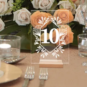 Detalle de número de mesa de acrílico transparente con base de madera y diseño floral.
