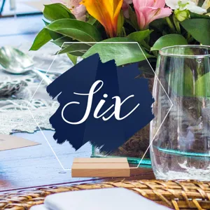 Detalle de tarjeta de número de mesa de acrílico con decoración floral y base de madera.
