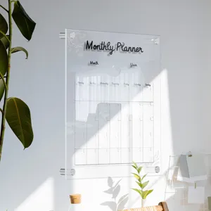 Clear acrylic monthly planner wall board detail showing weekly schedule grid and modern decor.
