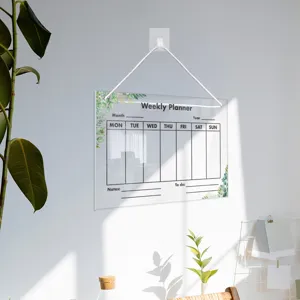 Detail view of a clear acrylic weekly planner board with green leaf design, hanging on wall.