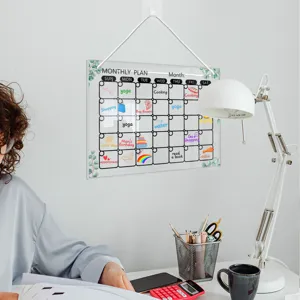 Clear acrylic monthly calendar hanging board detail in bright workspace setup with desk lamp.