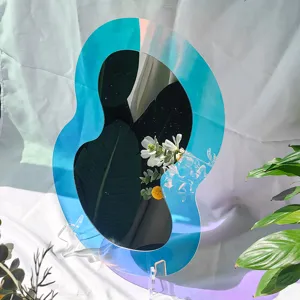 Détail de miroir acrylique iridescent, forme irrégulière avec bordure bleue et support.