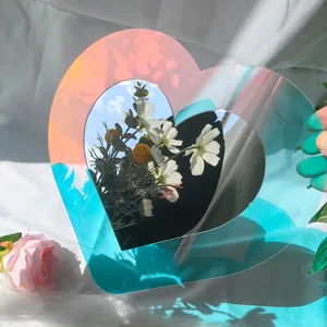 Détail de miroir en acrylique irisé en forme de cœur avec reflets holographiques et fleurs.