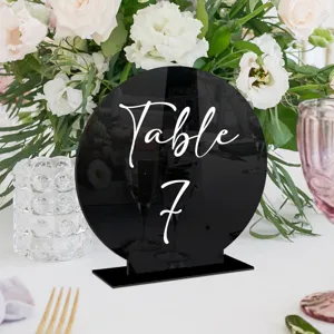 Vista detallada del cartel de mesa de boda redondo de acrílico negro con texto blanco.
