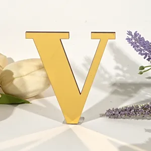 Gedetailleerde close-up opname van gouden spiegel acryl letter V decoratie met mooie bloemen.