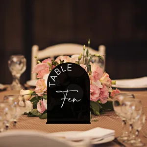 Close-up of black arch acrylic wedding table number sign with elegant floral backdrop.