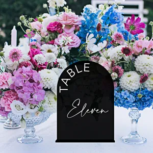 Detail shot of a black acrylic table number sign with elegant white text, wedding decor setup.