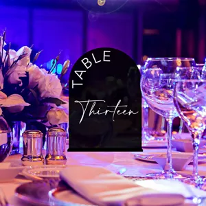 Detailed view of black arched acrylic table number sign set in wedding dinner scene.