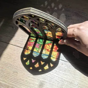 Wooden stained glass window suncatcher ornament, arched gothic window design casting colorful light shadows.