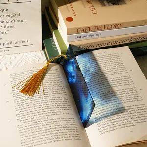 Close-up of translucent dragon acrylic bookmark with yellow tassel resting on open book.