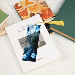 Close up of a blue transparent acrylic dragon bookmark with a delicate gold tassel on books.