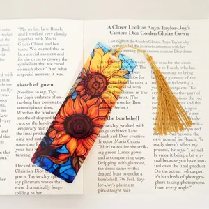 Close-up of a translucent acrylic sunflower bookmark with a golden tassel on an open book.