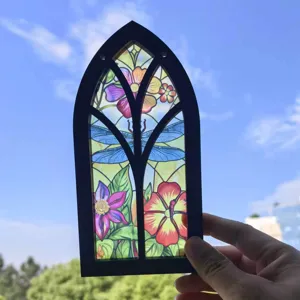 Detailed view of gothic arched stained glass window hanging with floral and dragonfly motifs.