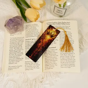 Acrylic dragon bookmark with gold tassel detail, placed on open book with flowers background.