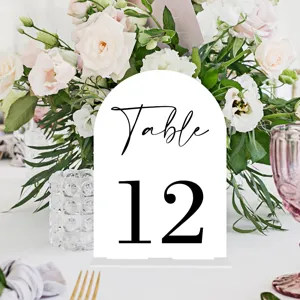 Detailed view of white arched acrylic table number sign with elegant floral wedding decor setup.
