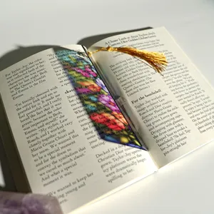 Close-up of colorful translucent acrylic bookmark with golden tassel inside book page.