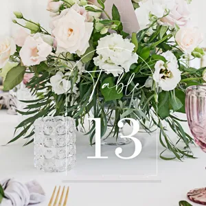 Clear arched acrylic wedding table number sign detail view with elegant floral backdrop