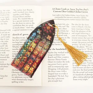 Detailed close-up of a colorful translucent acrylic bookmark with a gold tassel on open book.