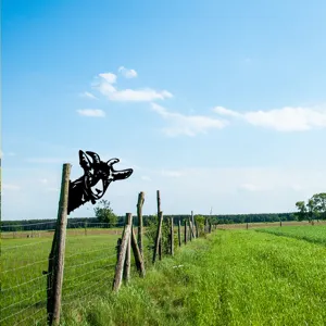 Metal goat silhouette garden stake shown installed on a wooden fence outdoors in field.