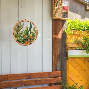 Close-up detail of the round wooden and metal cactus wall hanging decor in outdoor scene.