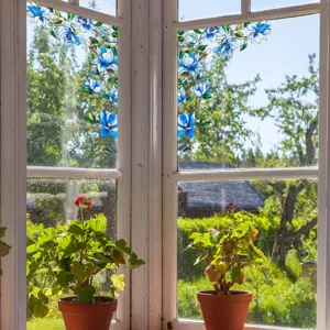 Detailed view of blue floral stained glass window film applied to window with potted plants.