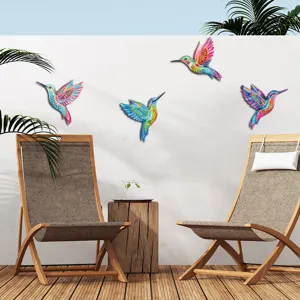 Colorful metal hummingbird wall art hanging on outdoor patio wall with wooden lounge chairs.