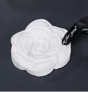 Detailed close-up shot of a white camellia plaster aroma pendant with a black ribbon.