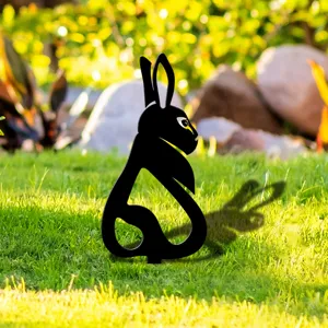 Vue détaillée d'une silhouette de lapin noire plantée dans l'herbe verte du jardin.