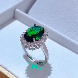 Primo piano dettagliato di un elegante anello con gemma verde ovale e zirconi scintillanti.