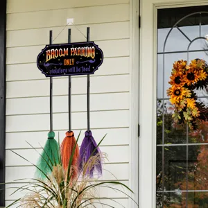 Halloween witch broom parking wooden sign detail view with colorful miniature brooms hanging decor.