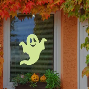 Halloween glowing ghost window hanging detail view with autumn leaves and pumpkin decor.