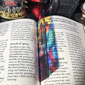 Detailed view of transparent stained glass style acrylic bookmark with red tassel inside book.