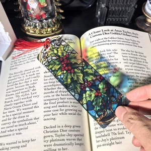 Transparent acrylic Christmas bookmark with red tassel, stained glass holly pattern detail view.