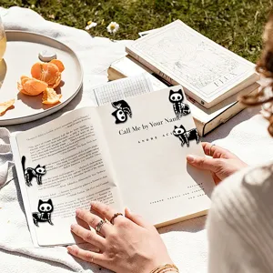 Close-up detail of cute black and white skeleton cat magnetic bookmarks clipped on open book.