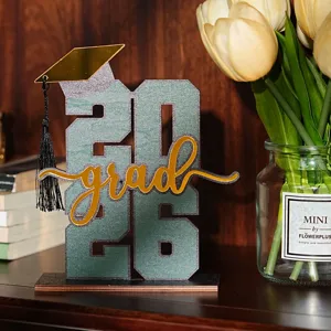 Dettaglio decorazione tavolo laurea in legno 2026, con scritta grad dorata e cappello.