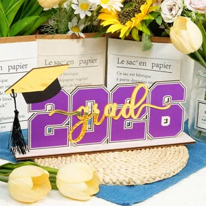 Centro tavola di laurea in legno 2026 con scritta grad dorata e cappello per la festa.