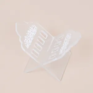 Close-up detail of a clear acrylic book stand with engraved Arabic script, minimalist desktop decor.